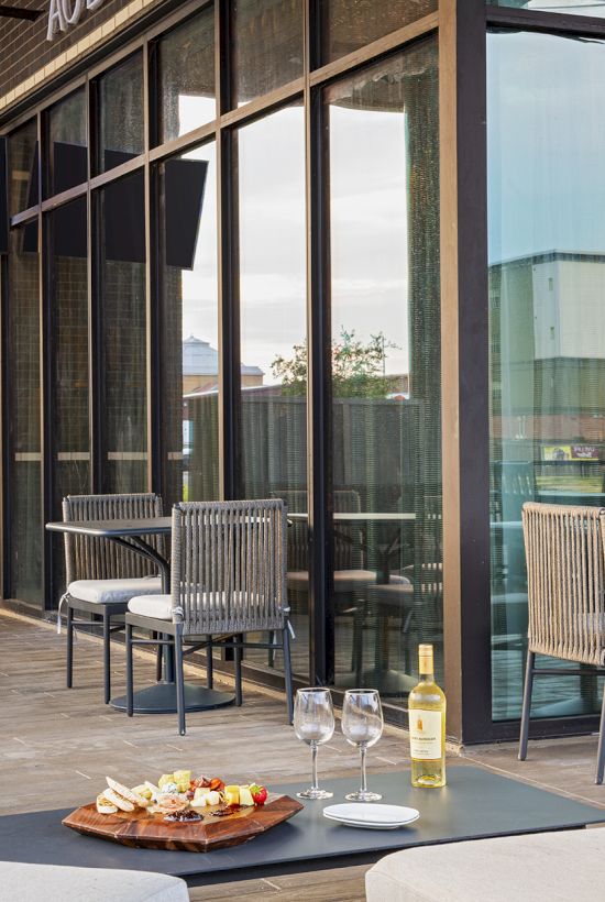 A cozy outdoor dining setup with two chairs, a small table, wine glasses, a plate of appetizers, and a bottle of wine on a patio.
