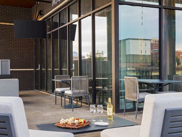 A cozy outdoor patio setup with a small table, wine bottle, glasses, and snacks, surrounded by modern glass doors and lounge chairs.