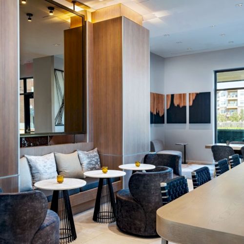 A modern living room with a mounted TV, cozy sofa, glass coffee table, and large windows bringing in natural light.