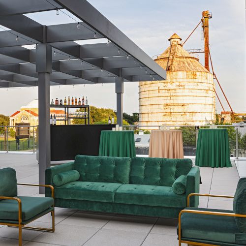 A cozy outdoor seating area with green couches and a small table under a covered patio, sunny and inviting.
