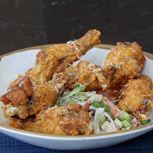 A plate of battered fried chicken pieces with dipping sauce, served on a white plate and dark table.