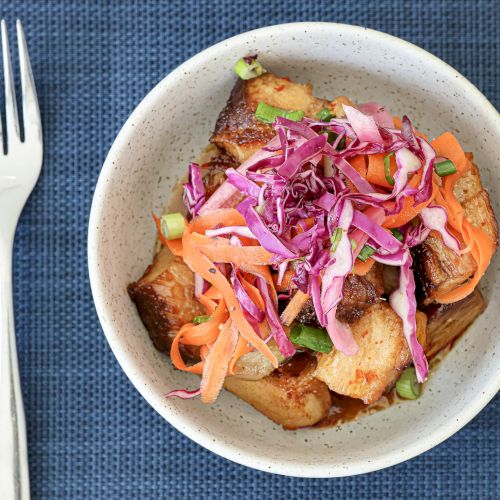 Small plate of pink-trothed meat or seafood salad with thin onion slices, cilantro, and a light sauce, on a white dish with a fork nearby.