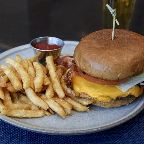 A hamburger with fries on a plate, close-up, savory bun and cheese, chips scattered around, brown sauce dots on the side.