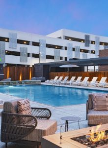 An outdoor hotel pool courtyard with lounge chairs, fire pit, and a &ldquo;WACO&rdquo; sign on a modern building under a blue sky.