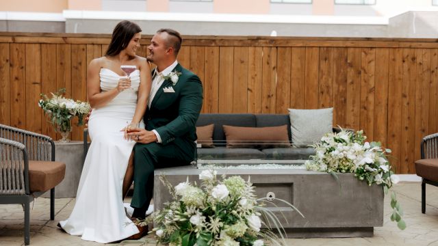A bride and groom in a venue clink champagne glasses, smiling at each other during their wedding celebration.